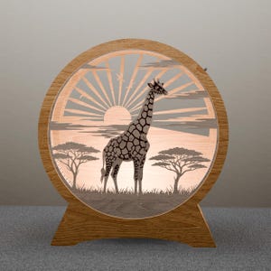 May include: Wooden, round lamp featuring a laser-cut design of a giraffe in an African savanna scene. The lamp has a warm, glowing light, with a sunrise and trees in the background. The lamp is supported by a wooden base.
