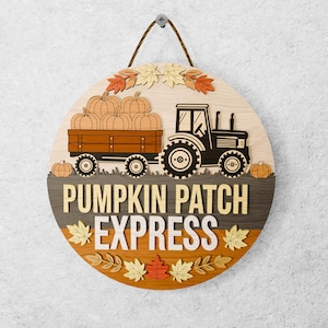 Puede incluir: Un letrero redondo de madera con temática otoñal. Muestra un tractor tirando de un vagón lleno de calabazas. Las palabras "PUMPKIN PATCH EXPRESS" están en capas. Hojas y calabazas decorativas rodean el diseño.