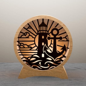 Puede incluir: Lámpara redonda de madera con temática náutica, con un diseño de faro y ancla. La lámpara tiene un interior cálido y brillante, con una silueta de faro, ancla, sol y olas. La lámpara está soportada por una base de madera.