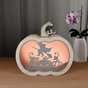May include: Wooden pumpkin-shaped Halloween decoration with a witch on a broom and carved jack-o'-lanterns. The interior has a copper-colored backing. The pumpkin has a wooden stem and is sitting on a wooden surface.