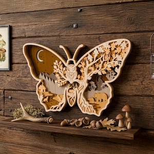 Peut inclure: Une œuvre d'art murale en bois en forme de papillon avec un design en couches. L'œuvre présente une scène de forêt avec un hibou, des ours, des arbres et un croissant de lune. L'œuvre est exposée sur un mur en bois avec une étagère contenant des objets décoratifs.