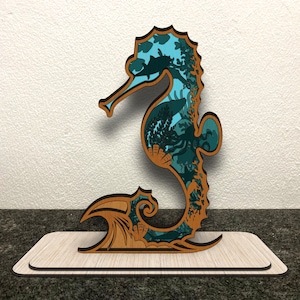 May include: A wooden seahorse sculpture with a blue and green design depicting an underwater scene. The seahorse is standing on a wooden base.
