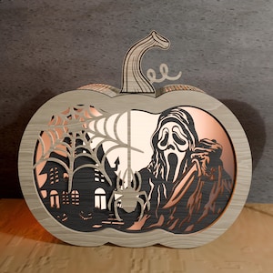 Puede incluir: Decoración de calabaza de Halloween de madera con un diseño en capas. La calabaza presenta un recorte de una casa embrujada, una telaraña y una figura de fantasma. El interior tiene un respaldo de color cobre.