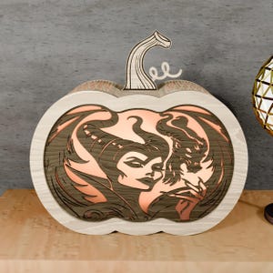 May include: Wooden pumpkin-shaped decorative piece with a light-colored frame and a dark wood interior. The interior features a layered design depicting a woman and a dragon in shades of brown and copper. The stem is light-colored wood.