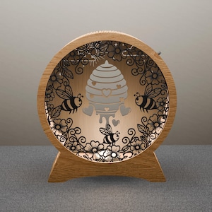 May include: A wooden, round decorative light with a bee and honeycomb design. The light features a laser-cut design of bees, flowers, and a honeycomb with heart accents. The light is made of wood and has a warm, inviting glow.