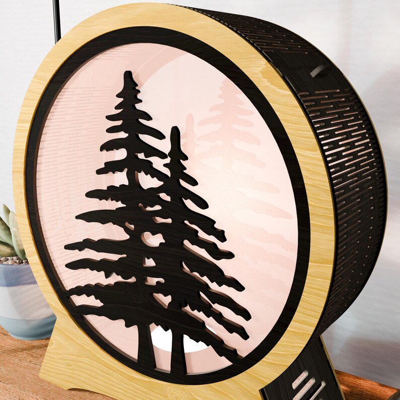 May include: A round wooden lamp with a black tree silhouette design. The lamp has a light pink background and a wooden base. The lamp's frame is made of light wood and black accents.