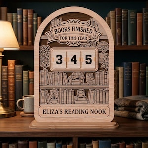 Könnte beinhalten: Leserechenbrett aus Holz in Form eines Bücherregals mit dem Text "BOOKS FINISHED FOR THIS YEAR" und der Zahl "345". Der untere Teil lautet "ELIZA'S READING NOOK". Das Design umfasst ein Bücherregal, einen Sessel und eine Eule.