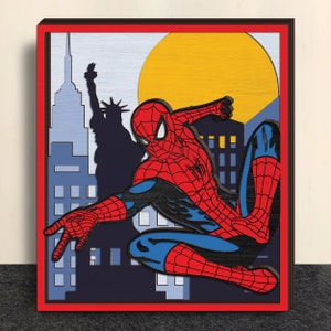 Op de afbeelding: Een houten kunstwerk in een frame met Spider-Man in een dynamische pose tegen een achtergrond van New York City. Het kunstwerk maakt gebruik van gelaagd hout om diepte te creëren, met een rood, blauw en zwart kleurenschema. De achtergrond bevat het Vrijheidsbeeld en een gele zon.