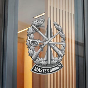 May include: A silver-colored emblem featuring a crossed saber, rifle, and other military equipment, surrounded by a laurel wreath. The words "MASTER GUNNER" are displayed on a black banner at the bottom of the emblem.