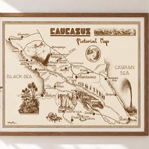 Op de afbeelding: Een ingelijste picturale kaart van de Kaukasusregio in bruine inkt op een crèmekleurige achtergrond. De kaart bevat geografische labels, bergafbeeldingen en stadsnamen zoals Bakoe, Tiflis en Batoemi, met de tekst Caucasus Pictorial Map.