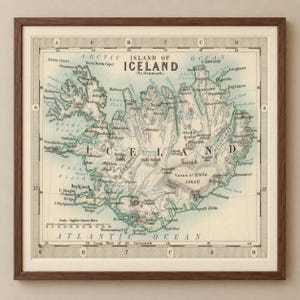May include: A framed vintage map of the Island of Iceland, featuring the text Island of Iceland (To Denmark), with detailed topography, coastal labels, a scale in statute miles, and a grid border, all encased in a dark brown wooden frame.