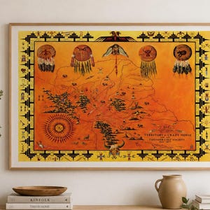 以下が含まれることがあります： 「Territory of Crazy Horse and the Thunder Colt Society 1847-1877」と題された地図が描かれた長方形の額入りプリント。地図はオレンジ色の背景で、動物、シンボル、太陽の黒いイラストが描かれており、黄色い枠で囲まれています。