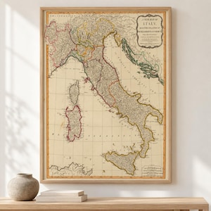 Op de afbeelding: Een ingelijste vintage-stijl kaart van Italië met de eilanden Sardinië en Corsica. De kaart toont geografische details in gedempte tinten met de tekst A NEW MAP OF ITALY, WITH THE ISLANDS OF SICILY, SARDINIA & CORSICA.