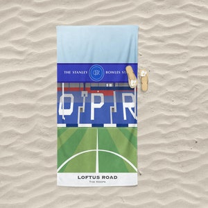 Könnte beinhalten: Ein blaues und weißes Strandtuch mit einer Grafik eines Fußballstadions, dem Text "Loftus Road" und "The Hoops" sowie dem Teamlogo. Das Handtuch liegt auf einem Sandstrand.