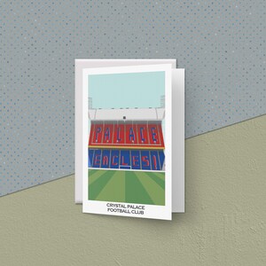 Könnte beinhalten: Eine Grußkarte mit einer stilisierten Illustration des Selhurst Park, der Heimat des Crystal Palace Football Club. Das Stadion ist rot und weiß mit den Worten "Palace" und "Eagles!" in blau.