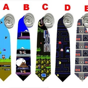 Puede incluir: Cinco corbatas novedosas con diseños temáticos de videojuegos. Las corbatas presentan gráficos pixelados de juegos clásicos, incluyendo Pac-Man y mandos de consola retro. Cada corbata tiene un esquema de color diferente, con diseños sobre un fondo azul, negro y gris.