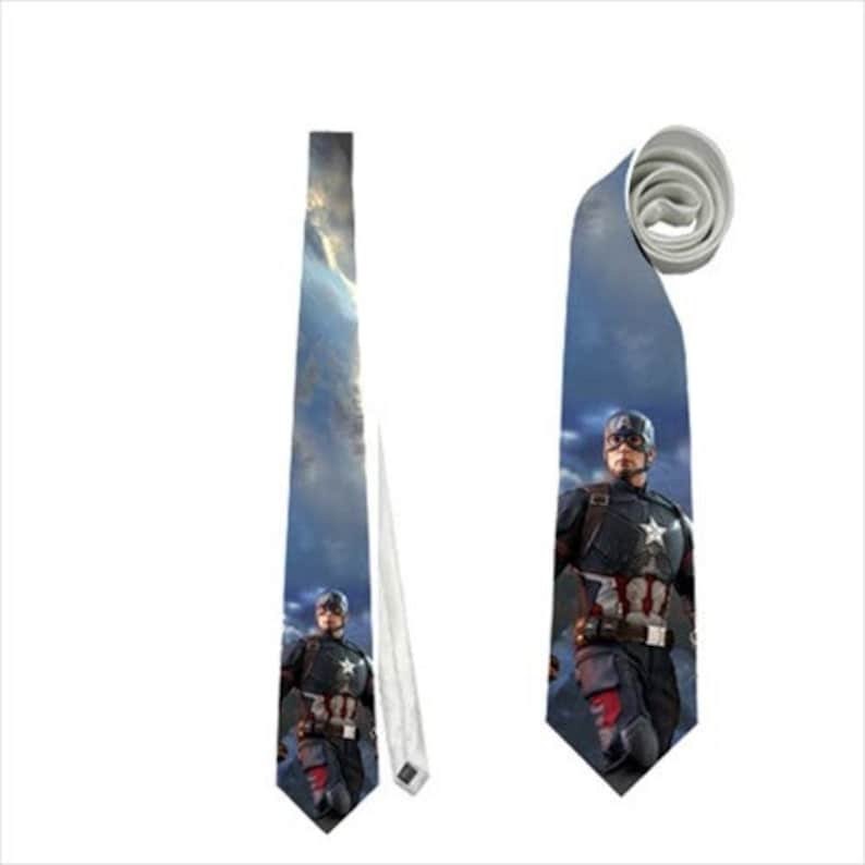 May include: Two neckties featuring Captain America. One tie is fully extended, displaying the character against a cloudy sky background. The other tie is rolled up, showing the character in a similar pose. Both ties have a white backing.