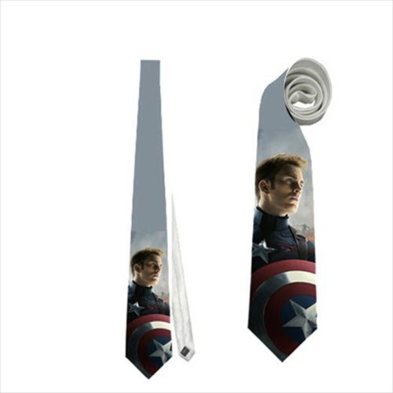 May include: A gray necktie featuring a portrait of a man in a navy blue uniform with a red, white, and blue shield. The tie is displayed flat and rolled, showcasing the design and fabric.