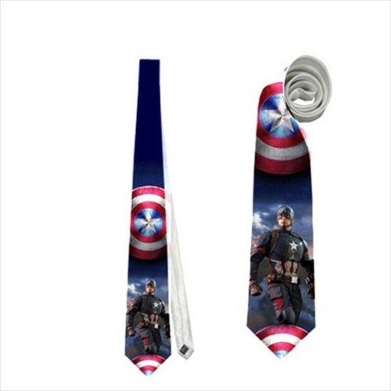 May include: A navy blue tie featuring Captain America's shield and a graphic of Captain America. The tie has a white reverse side and a pointed tip. The shield design is red, white, and blue.