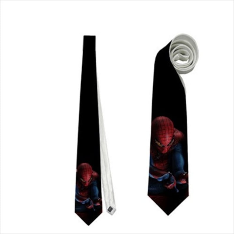 May include: Black necktie featuring a Spiderman graphic. The tie shows Spiderman in his red and blue suit against a dark background. The tie is displayed both flat and rolled, showcasing the design.