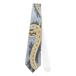 May include: A necktie with a unique design. The tie features a light gray background with dark gray brushstrokes. A gold-colored, stylized snake design with black and white accents is prominently displayed on the tie.