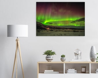 Puede incluir: Una impresión de arte mural rectangular que muestra una vibrante aurora boreal con rayas de luz verde brillante y púrpura intenso sobre un paisaje oscuro y nevado y una cadena montañosa bajo un cielo estrellado.