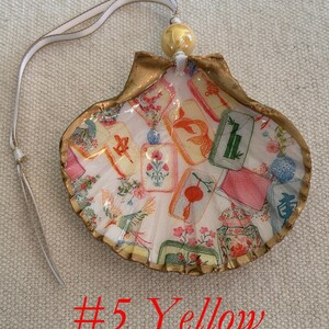 May include: A decorative seashell ornament with a gold-painted edge, featuring a colorful design of floral and card motifs. It has a white ribbon for hanging and a yellow bead at the top. The text "#5 Yellow" is visible.