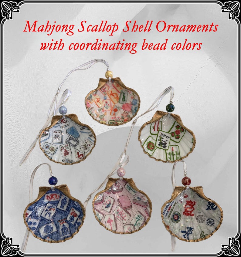 May include: Six scallop shell ornaments with coordinating bead colors. Each shell is painted with a different Mahjong tile design. The shells are trimmed in gold and have a white ribbon for hanging. The text "Mahjong Scallop Shell Ornaments with coordinating bead colors" is at the top.