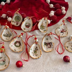 May include: A set of twelve oyster shell ornaments, each featuring a unique hand-painted Christmas illustration and a gold-painted edge. Each shell is numbered from one to twelve and includes a red ribbon loop for hanging, accented with small red beads.