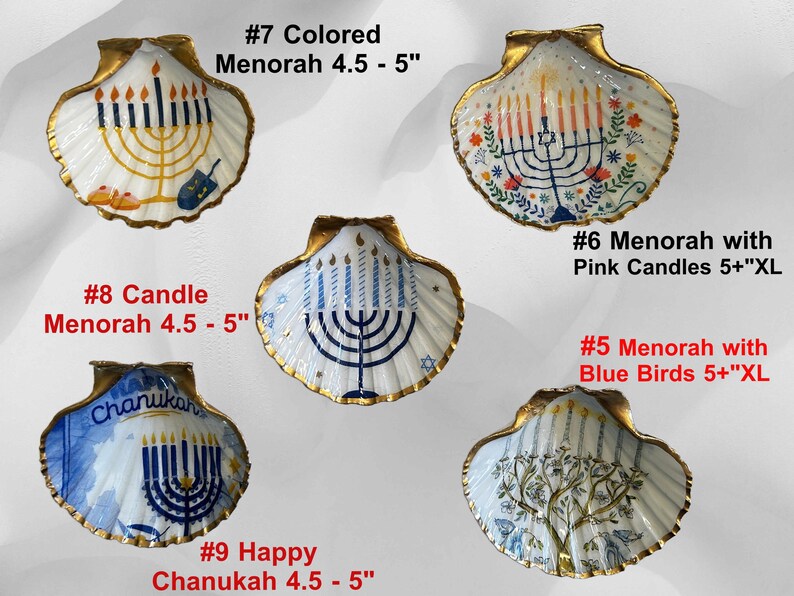 May include: A set of three ceramic mugs with a speckled, cream-colored glaze. Each mug features a different hand-painted design: a blue and green leaf, a yellow flower, and a red berry. The mugs have a simple, modern design.