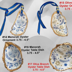 May include: Oyster shell ornaments and dishes with blue and gold accents. The ornaments have blue ribbons for hanging. Designs include menorahs, olive branches, and stars. Sizes range from 3.75 to 4.5 inches.