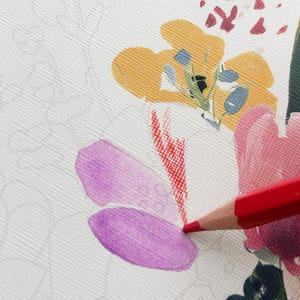 May include: A red colored pencil is used to color a floral illustration on textured white paper. The drawing features a yellow flower, a pink flower, and a purple petal, with additional faint gray outlines of uncolored floral stems and leaves.