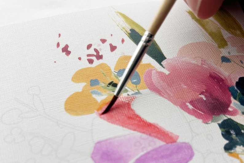 May include: A paintbrush with a light wood handle and silver ferrule applies red paint to a textured white canvas. The canvas features a partially completed floral illustration with yellow, pink, purple, and dark blue painted shapes and outlines.