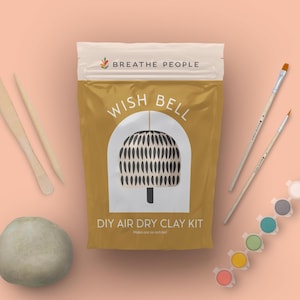 May include: A DIY air dry clay kit with the text "Wish Bell" and "Breathe People". The kit includes a bag, clay, paintbrushes, paint, and tools. The kit makes one six inch bell. The background is a light pink color.