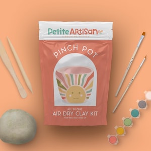 May include: A craft kit for kids, featuring a bag with "Pinch Pot" text and a sun design. The kit includes clay, paintbrushes, wooden tools, and paint. The text "Air Dry Clay Kit" is also visible.