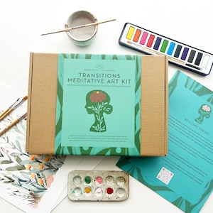 May include: A craft kit with the text "Transitions Meditative Art Kit" on the box. The kit includes watercolor paints, brushes, a ceramic bowl, and a palette with paint. The kit is designed for honoring transitions, shifting, and reframing.