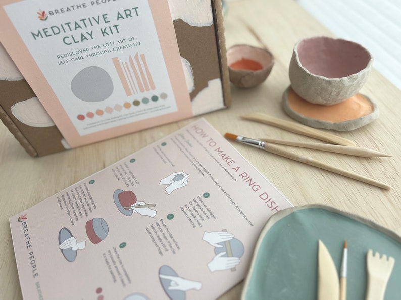 May include: A craft kit for making clay art. The box has a pink and brown design with the text "Meditative Art Clay Kit" and "Rediscover the lost art of self care through creativity". The kit includes tools, clay, and instructions for making a ring dish.