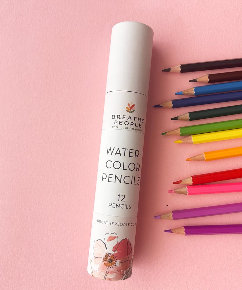 May include: A white cylindrical cardboard tube labeled BREATHE PEOPLE WATERCOLOR PENCILS 12 PENCILS with a floral illustration at the base. Twelve sharpened watercolor pencils in various colors are arranged in a fan shape next to the tube.