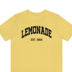 以下が含まれることがあります： レモンイエローの半袖Tシャツに、黒い文字で「LEMONADE EST. 2016」と書いてあります。