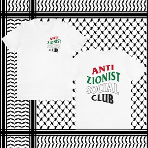 May include: White t-shirt with the text "ANTI ZIONIST SOCIAL CLUB" in red, green, and black letters. The letters are stacked on top of each other and are slightly curved. The shirt is on a black and white checkered background.