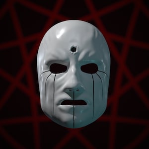 Puede incluir: Una máscara blanca con marcas negras alrededor de los ojos y la boca. La máscara tiene un solo punto negro en el centro de la frente.