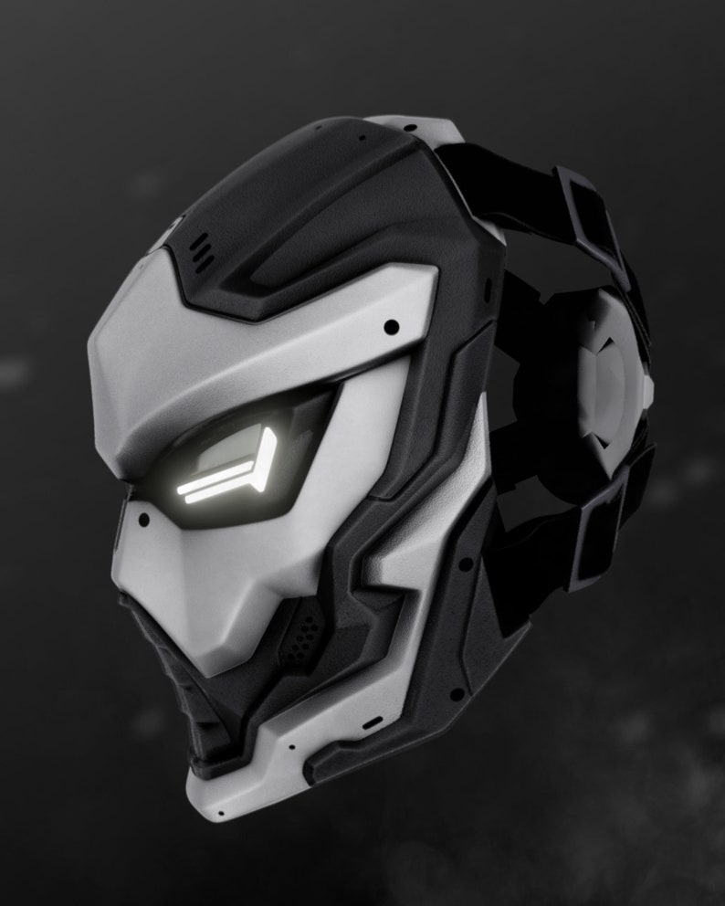 May include: A futuristic-looking silver and black helmet with a white light on the front. The helmet has a strap on the back and a textured design.