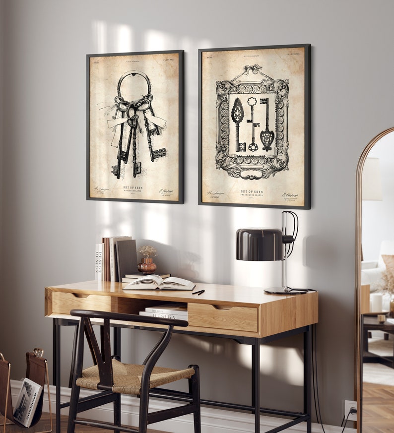 May include: Two black framed prints of vintage illustrations of keys. The prints are hanging on a light gray wall above a wooden desk with a black chair and a black lamp.