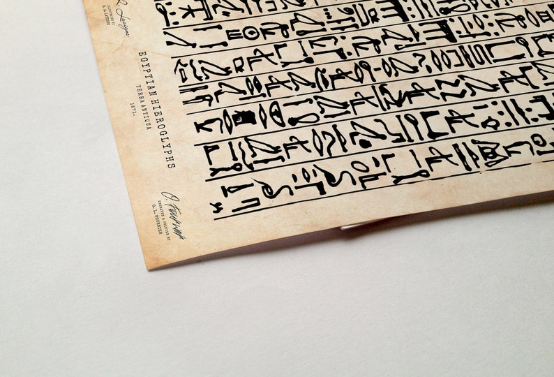 Peut inclure: Un papier vintage de couleur cr&egrave;me avec de l'encre noire repr&eacute;sentant des hi&eacute;roglyphes &eacute;gyptiens. Le texte "EGYPTIAN HIEROGLYPHS" est imprim&eacute; verticalement sur le c&ocirc;t&eacute; gauche du papier. Le texte "LIBRA ANTIOUA" est imprim&eacute; en dessous. Le texte "SEPTL." est imprim&eacute; en dessous. Le papier est l&eacute;g&egrave;rement enroul&eacute; dans le coin inf&eacute;rieur droit.