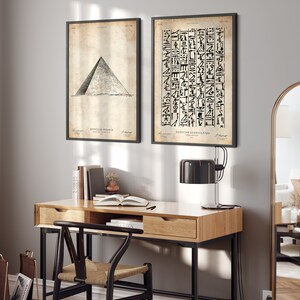 Peut inclure: Deux impressions en noir et blanc encadr&eacute;es sur un mur gris clair. L'impression de gauche montre un dessin d'une pyramide &eacute;gyptienne. L'impression de droite montre une colonne de hi&eacute;roglyphes &eacute;gyptiens. Les impressions sont accroch&eacute;es au-dessus d'un bureau en bois avec un cadre en m&eacute;tal noir. Une lampe noire est pos&eacute;e sur le bureau.