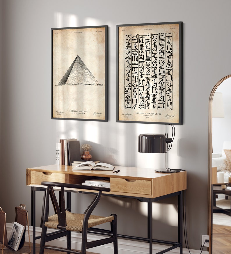 Peut inclure: Deux impressions en noir et blanc encadr&eacute;es sur un mur gris clair. L'impression de gauche montre un dessin d'une pyramide &eacute;gyptienne. L'impression de droite montre une colonne de hi&eacute;roglyphes &eacute;gyptiens. Les impressions sont accroch&eacute;es au-dessus d'un bureau en bois avec un cadre en m&eacute;tal noir. Une lampe noire est pos&eacute;e sur le bureau.