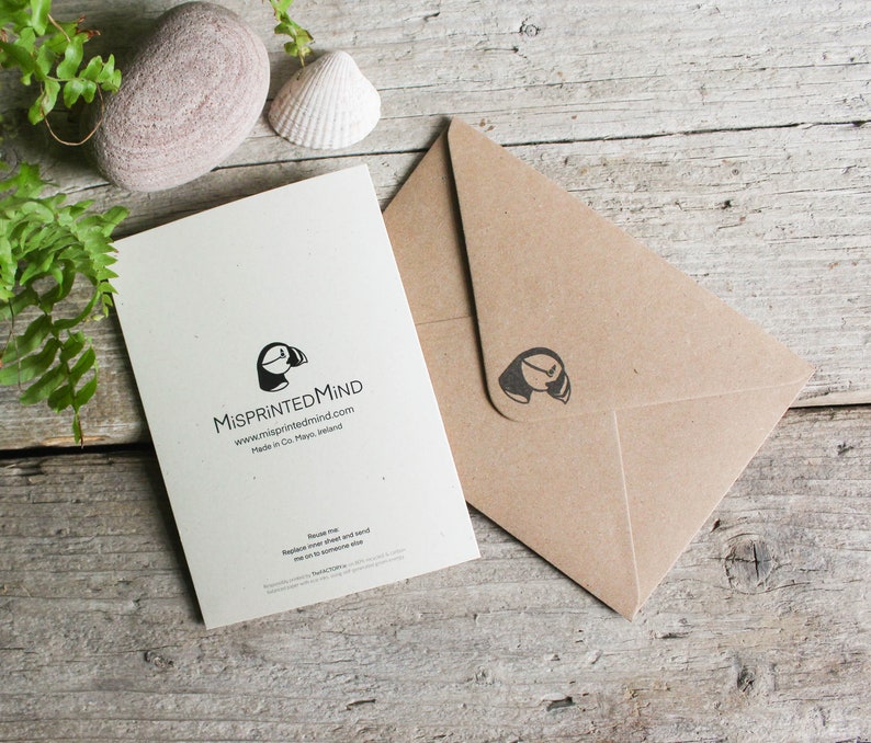 Pu&ograve; includere: Un biglietto bianco con un'illustrazione in bianco e nero di un puffin e il testo "MisprintedMind" e "www.misprintedmind.com". Il biglietto &egrave; su una superficie di legno con una busta marrone accanto.