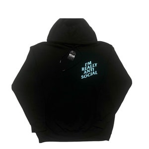 Puede incluir: Sudadera con capucha negra con el texto "I'M REALLY ANTI SOCIAL" en azul claro en la espalda. La sudadera tiene una capucha con cord&oacute;n y una etiqueta adjunta. La prenda est&aacute; hecha de un material suave.
