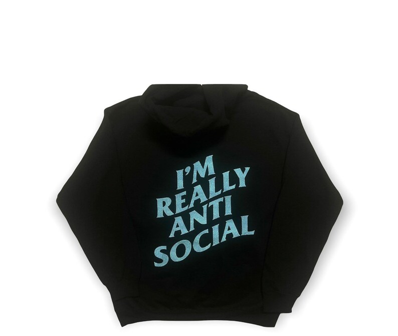 Puede incluir: Sudadera con capucha negra con el texto "I'M REALLY ANTI SOCIAL" en azul claro en la espalda. La sudadera tiene capucha y mangas largas. El fondo es blanco.
