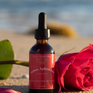 May include: A brown glass bottle with a black dropper, labeled "Taboo Aphrodisia FOR WOMEN" sits on sand next to a red rose. The bottle contains 2 oz (60 ml) of product.